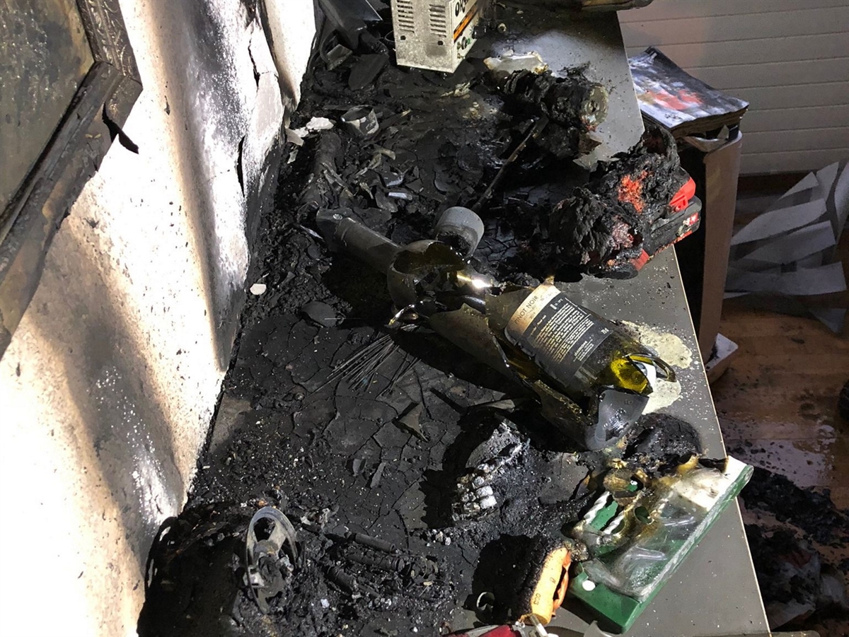 Auf der Oberseite eines Möbels liegen verbrannten und verkohlten Gegenstände. Darunter auch ein Aluminiumbehälter von einem Teelicht.