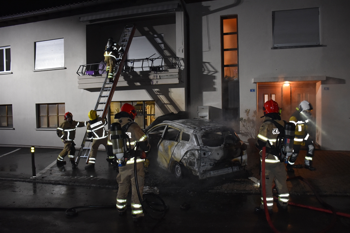 Feuerwehrleute mit dem rauchenden Auto vor dem Haus und mit Leiter
