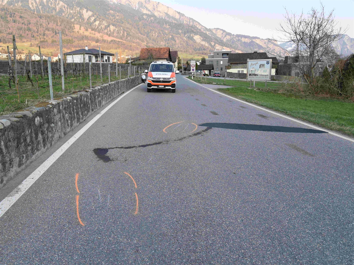 Die Fläscherstrasse mit Kratz- und Flüssigkeitsspuren des Unfalls sowie einem Polizeiauto. Im Hintergrund Berge und Horizont.