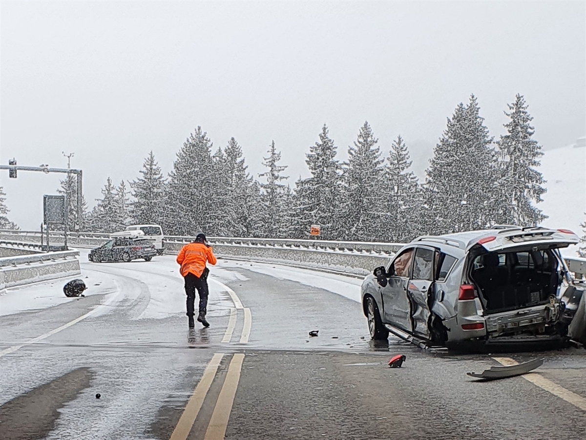 Rechts das total beschädigte talwärts fahrende Auto auf der winterlichen Fahrbahn. Links davon ein Polizist und etwas weiter in der Ferne die beiden anderen beteiligten Autos.