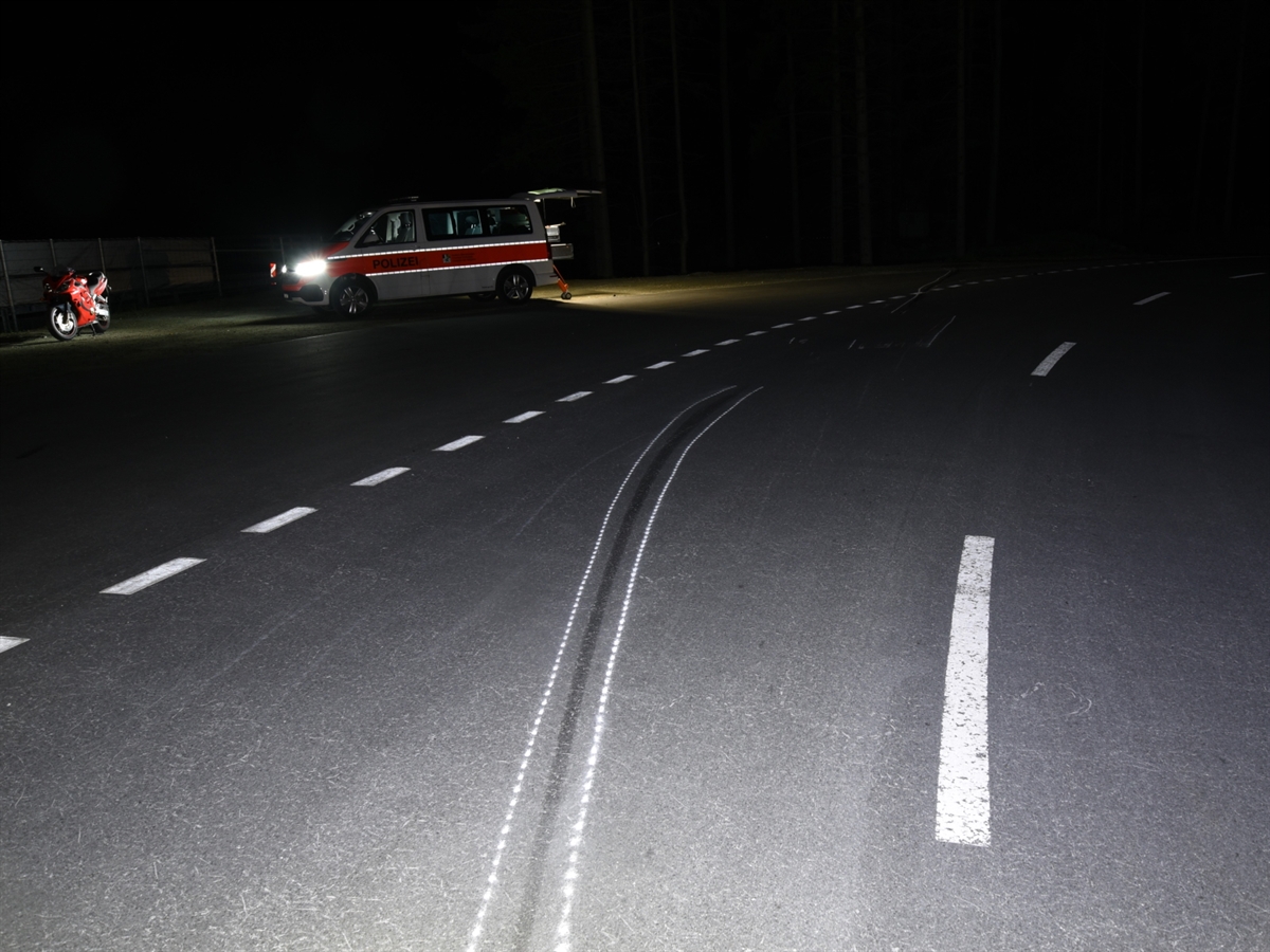 Nachtbild. Auf der Strasse ist eine Bremsspur eingezeichnet. Links davon stehen das verunfallte Motorrad sowie ein Patrouillenfahrzeug der Polizei.