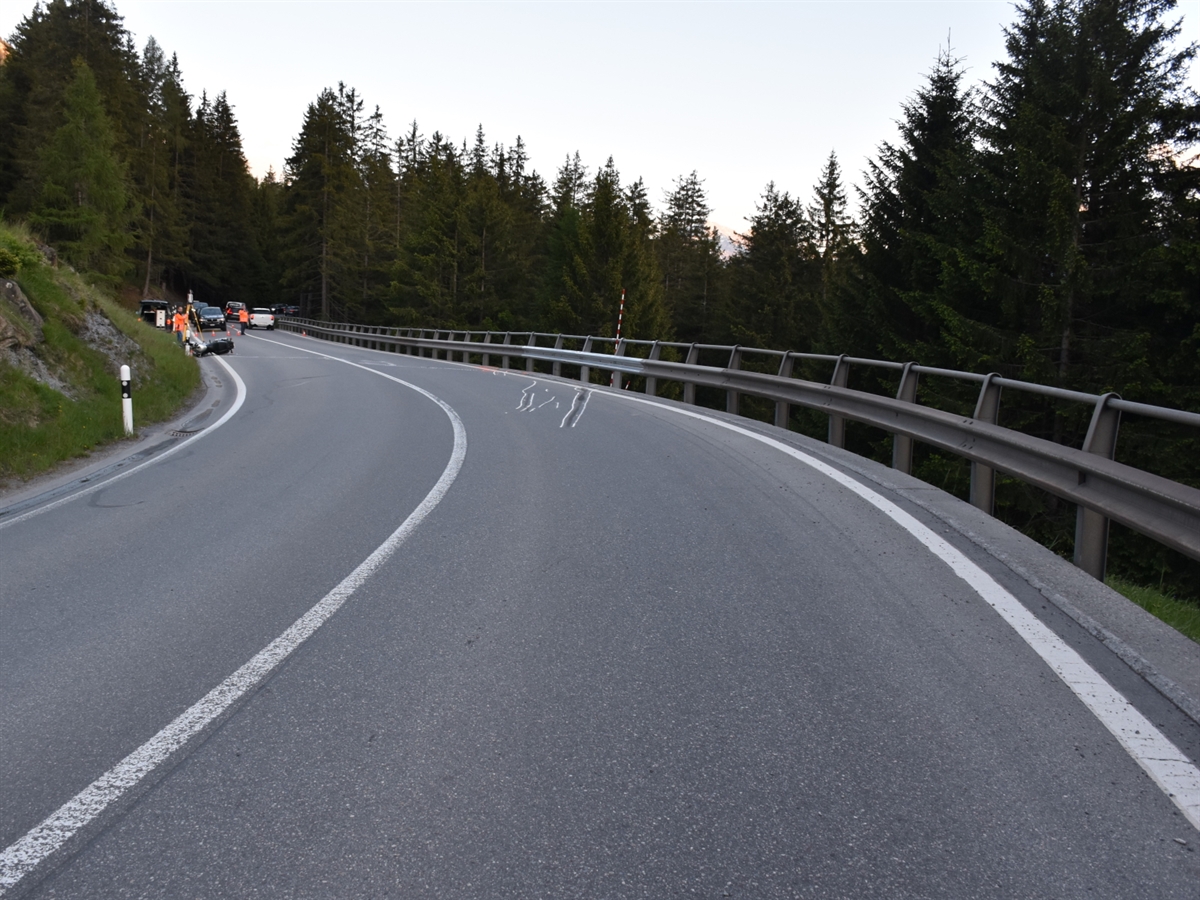 Die Linkskurve mit Sturzspuren nach rechts in Richtung der Leitplanke. Links weiter entfernt Einsatzkräfte und das am Boden liegende Motorrad.