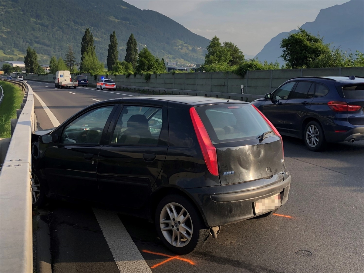 Links das mit der Front an der Mittelleitplanke stehende Unfallauto. Im Hintergrund Berge, auf der Autobahn einige weitere Fahrzeuge sowie auf dem Pannenstreifen ein Patrouillenfahrzeug.