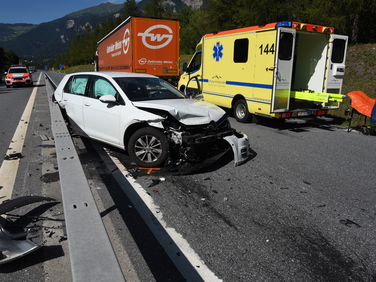 Rechts ein Ambulanzfahrzeug mit offenen Hecktüren. Links davon mit umgedrehter Front das total beschädigte Auto an der Leitplanke. Ein wenig weiter entfernt das Sattelmotorfahrzeug und auf der Gegenspur ein Polizeiauto.