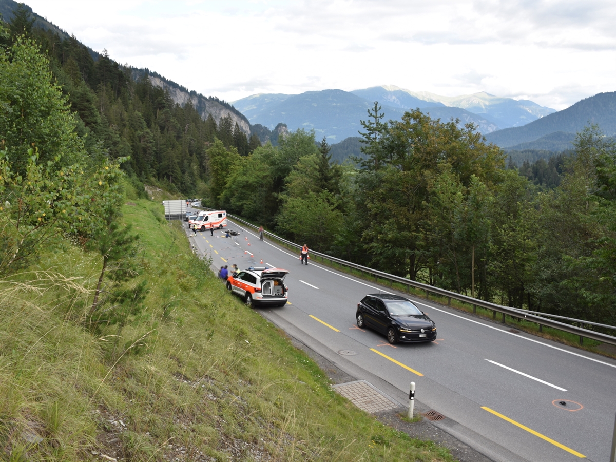 In der unteren Bildhälfte steht das beteiligte Auto sowie ein Patrouillenfahrzeug der Kapo auf der Unfallstelle. In der oberen Hälfte steht ein Ambulanzfahrzeug quer auf der Fahrbahn und vor diesem das verunfallte Motorrad.