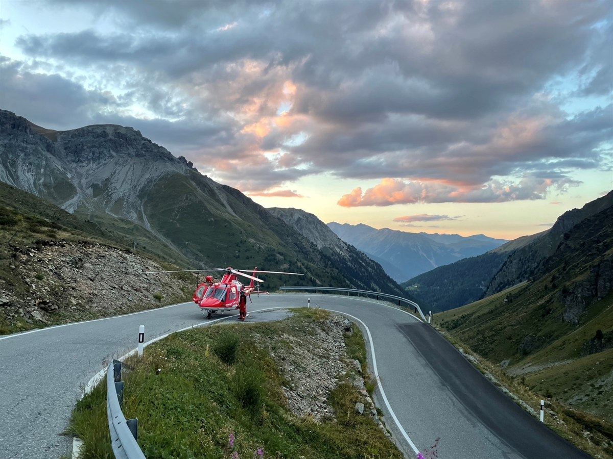 Abendstimmung am Umbrailpass mit einem Rega-Helikopter und dem Piloten daneben.