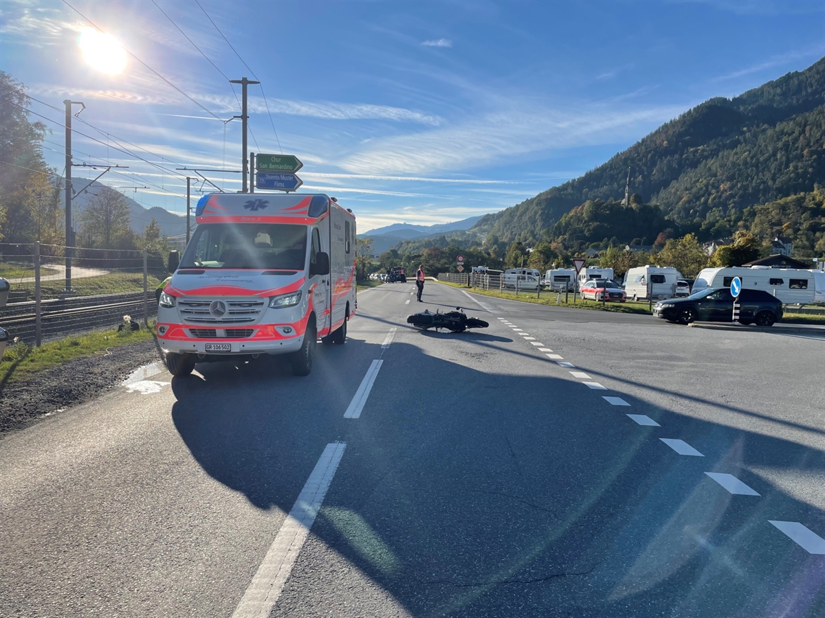Sonniges Herbstbild der Verzweigung Vial in Domat/Ems. Auf der Fahrbahn liegt ein Motorrad auf der Seite und links daneben steht ein Ambulanzfahrzeug. Eine Polizistin regelt den Fahrzeugverkehr an der Unfallstelle vorbei.