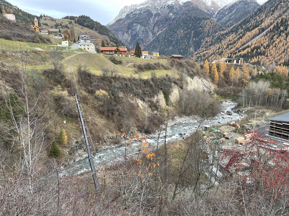Auf dem Bild ist die Örtlichkeit zu sehen, wo der Mann gefunden werden konnte. Man sieht den Bach Brancla, Wiesland, Bäume, einige Häuser von Ramosch und die Bergwelt.