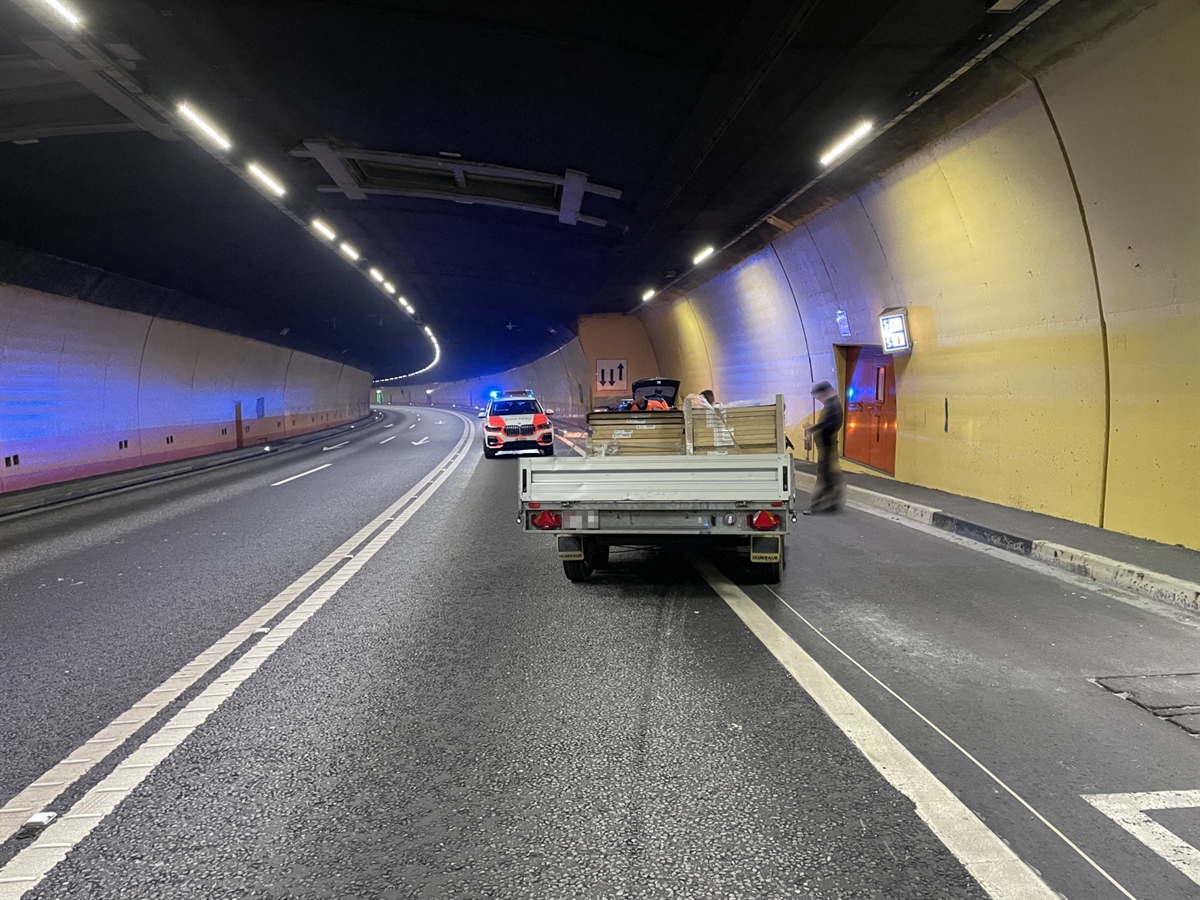 Der Anhänger von hinten, er steht halb auf der Strasse und halb in einer Notfallbucht. Im Hintergrund ein Polizeiauto mit eingeschaltetem Blaulicht.