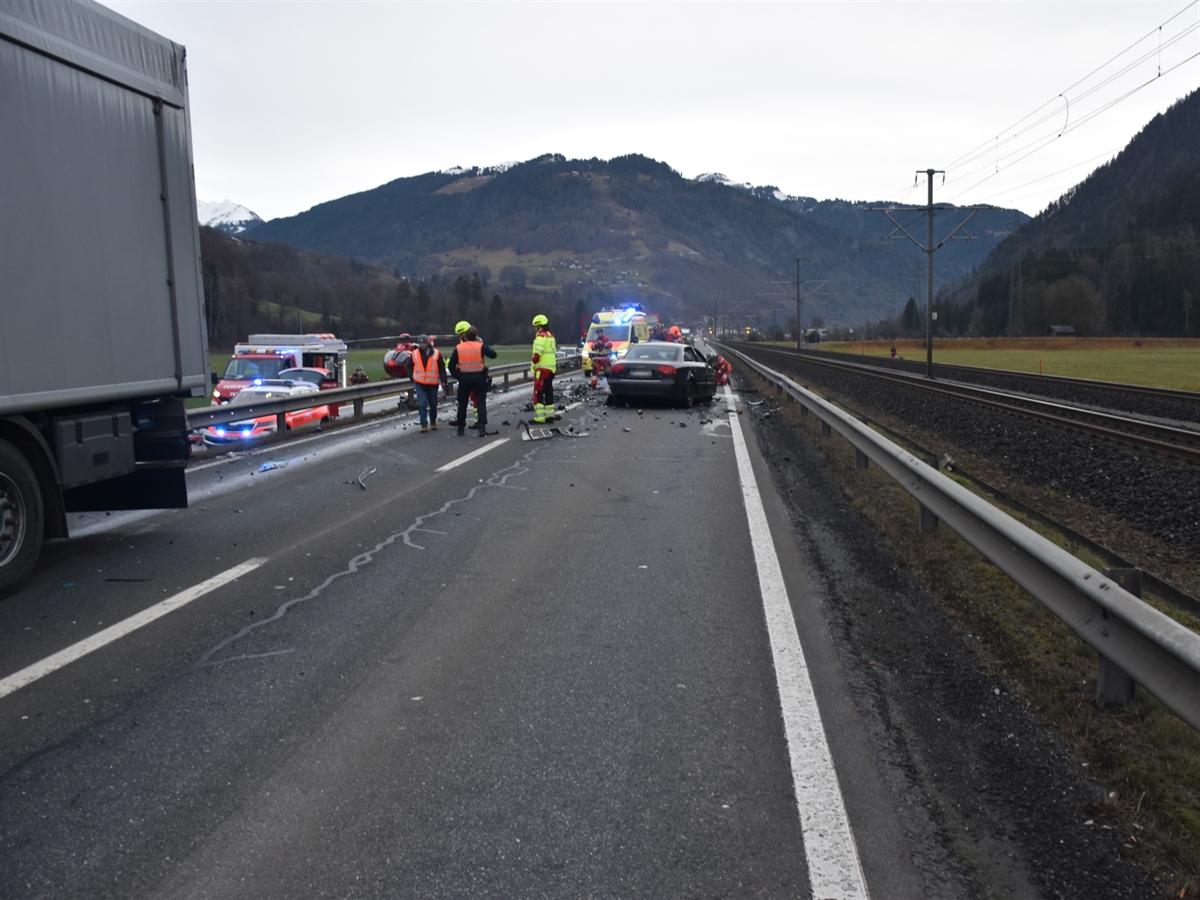 Links das Heck des Sattelanhängers, rechts davon Einsatzkräfte und auf der rechten Fahrspur das Auto von hinten. Weiter im Bild sind diverse Einsatzfahrzeuge und ein Rega-Helikopter.