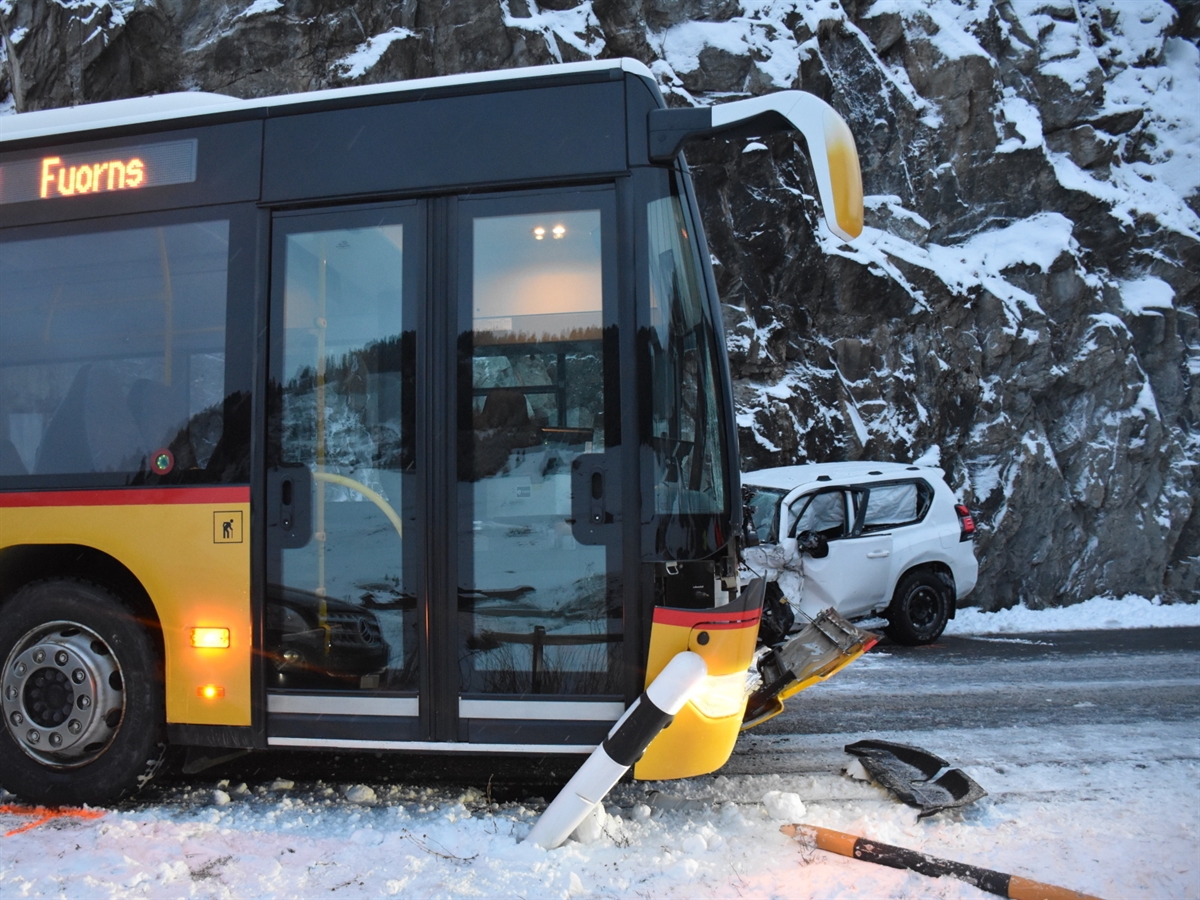 Die verschneite Strasse. Links das Postauto mit beschädigter Front. Dahinter ein frontal total beschädigtes weisses Auto. 