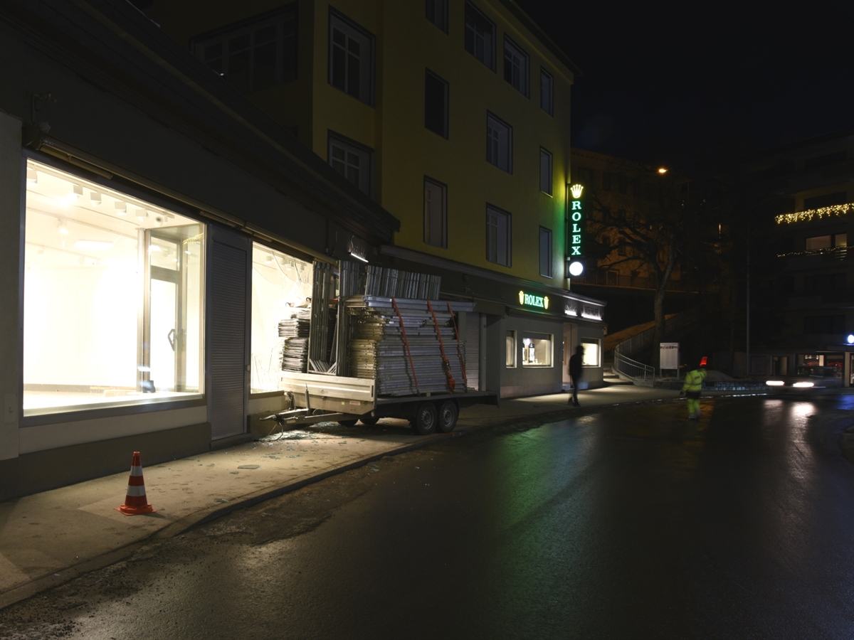 Blick auf die Strasse. In Bildmitte der auf dem Trottoir stehende Anhänger von vorne. Links davon die Immobilie mit total beschädigtem Schaufenster. 