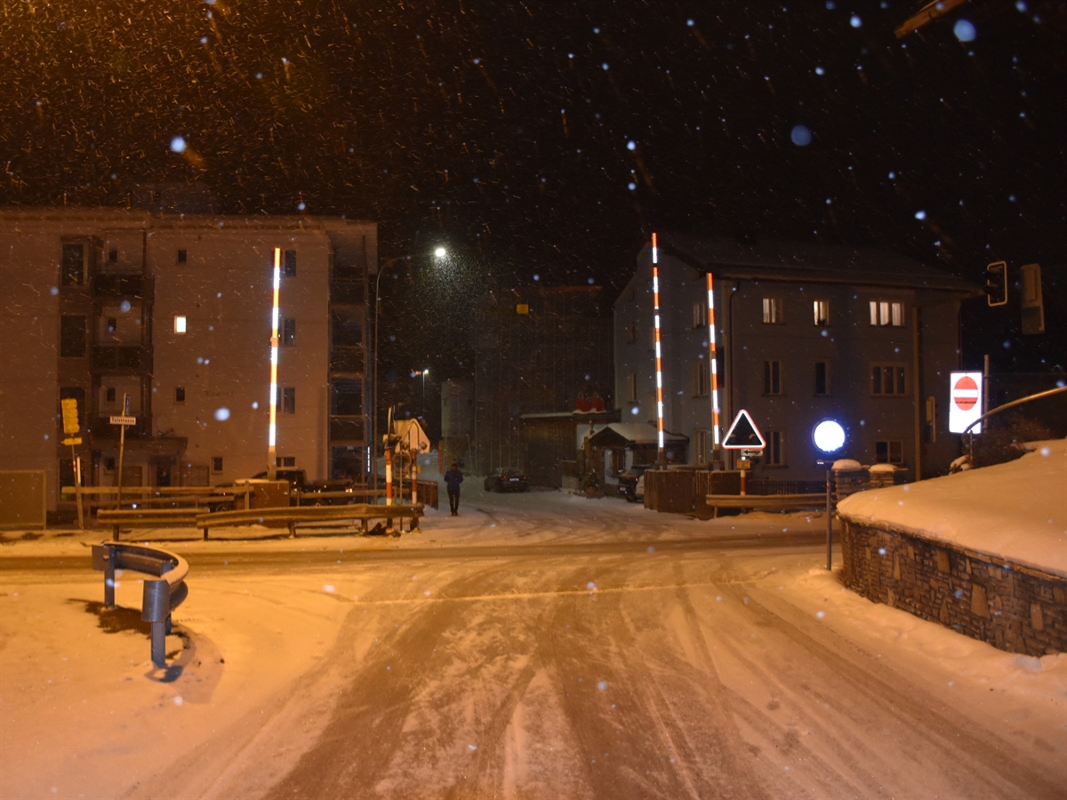 Dischmakreuzung in Richtung Talstrasse gesehen. Es herrscht leichter Schneefall und die Strasse ist dementsprechend schneebedeckt. Die Die Strassenbeleuchtung verschönert die Nach mit einem warmen Licht.