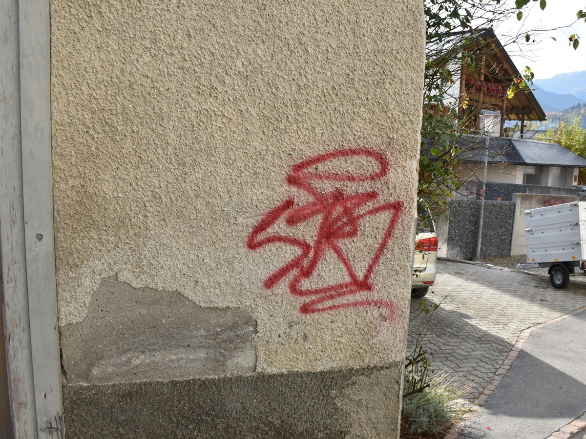 Rechts ein Vorplatz und ein Haus, links eine durch rote Farbe verschmierte Hauswand.