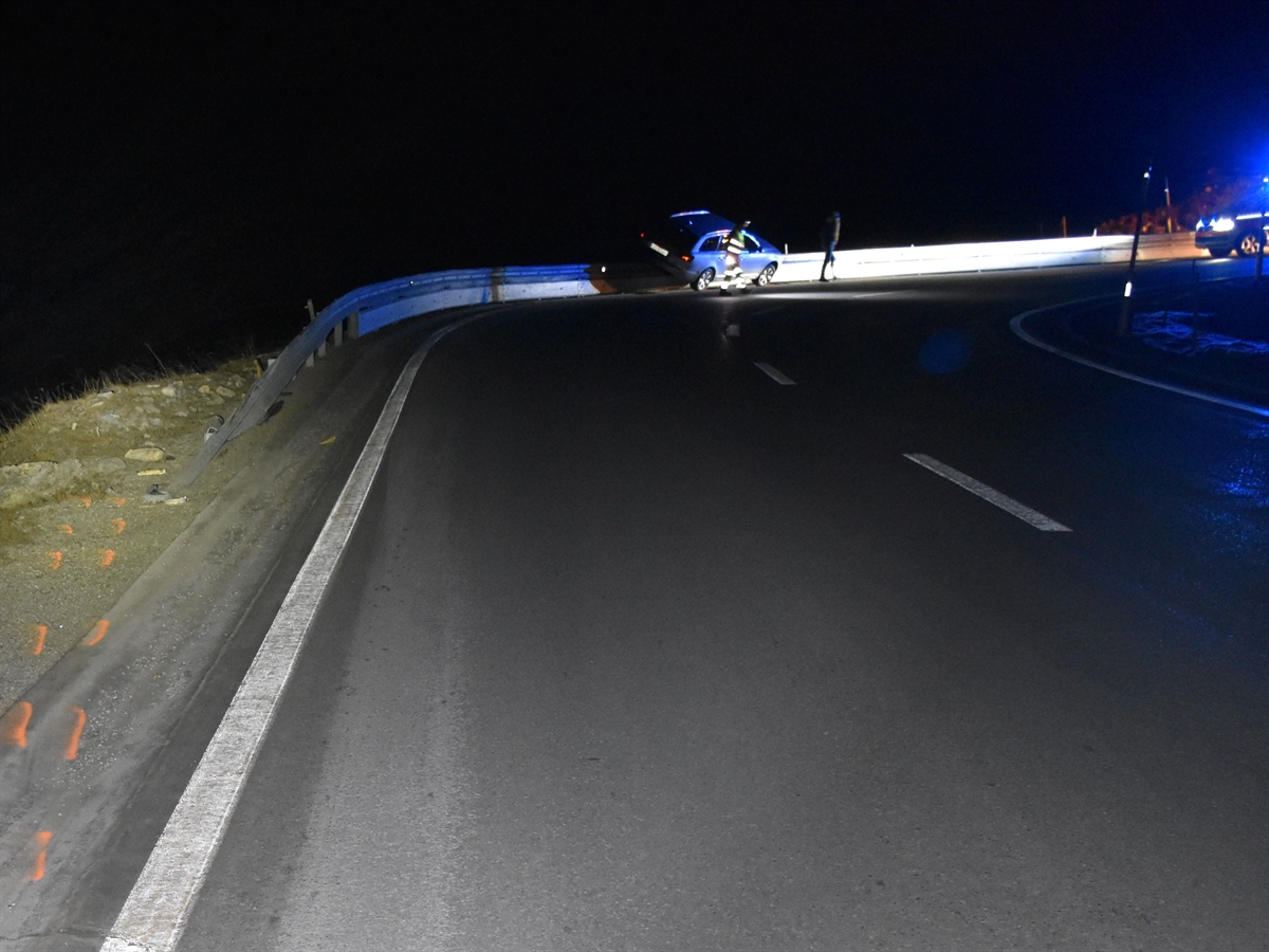 Aufnahme in der Dunkelheit. Das Auto steht mit der linken Seite auf der Leitplanke und mit den rechten Rädern auf der Strasse. Rechts davon die Front eines Polizeiautos.