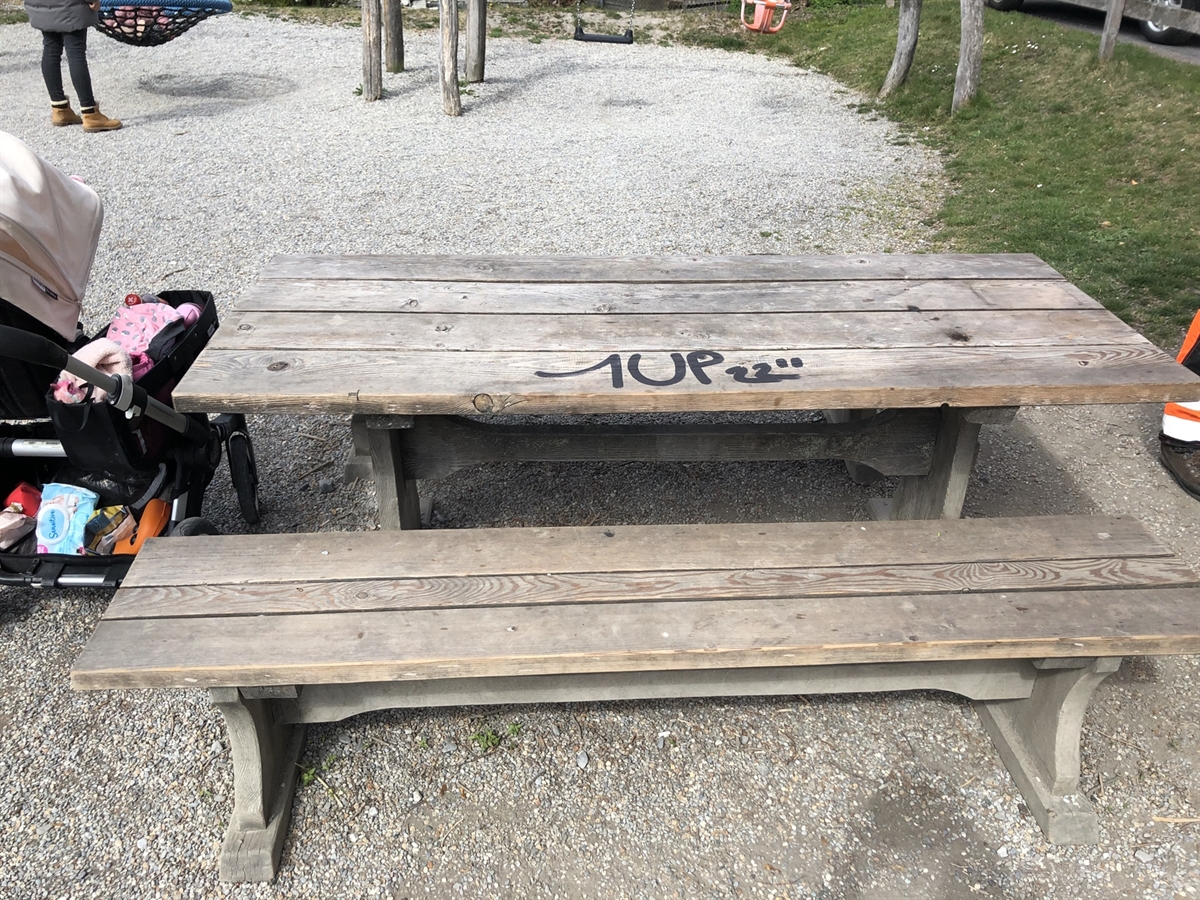 Sprayerei an einem Tisch bei einem Kinderspielplatz. Links neben dem Tisch steht ein Kinderwagen.