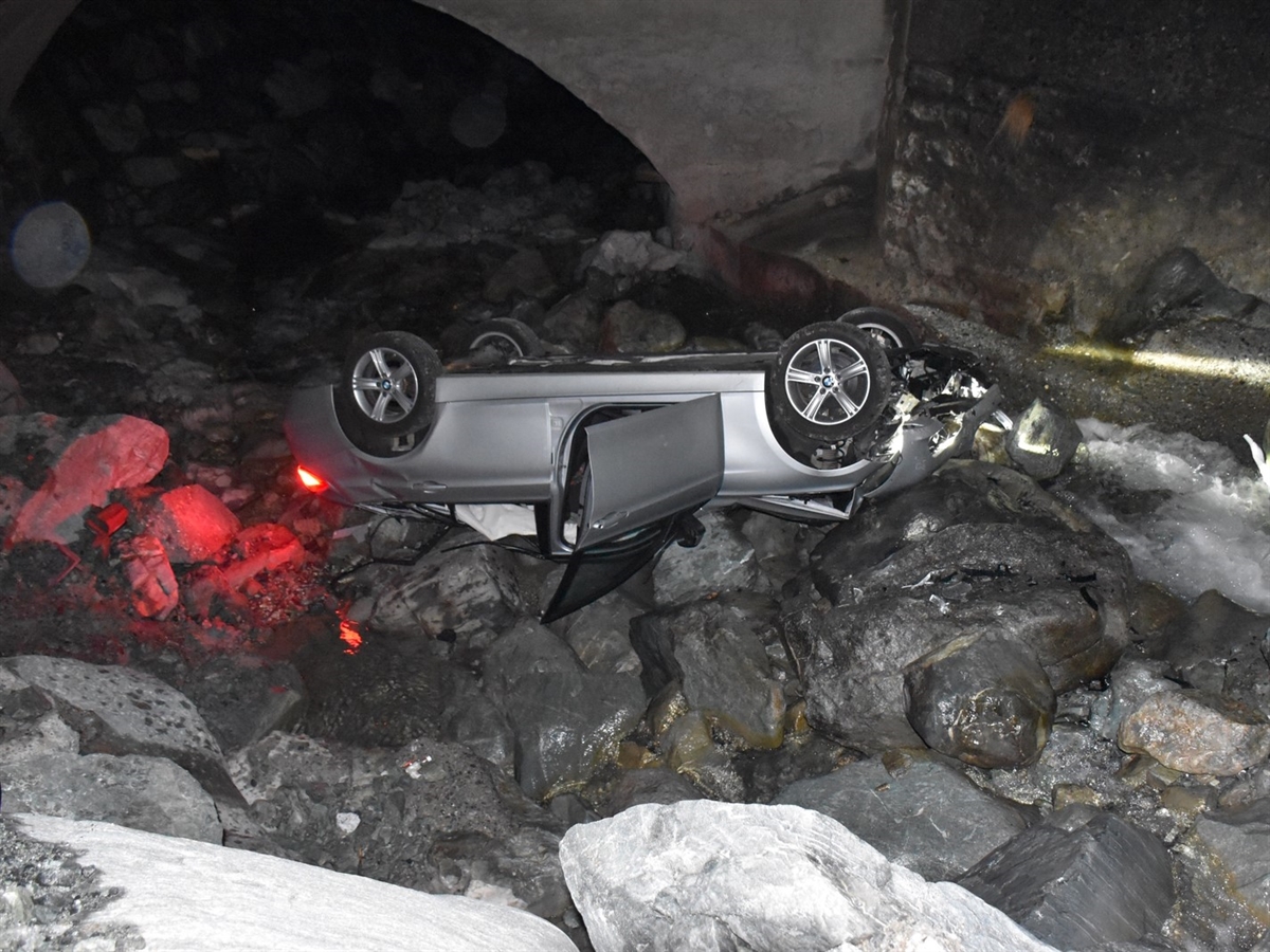Das silbergraue Auto liegt inmitten des Bachbetts. Im Hintergrund die Brücke. 