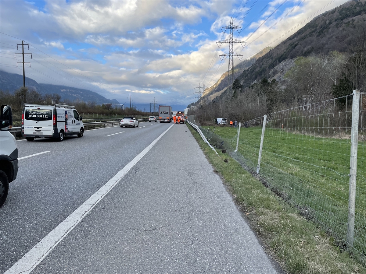 Die Südspur der A13. Rechts der beschädigte Wildschutzzaun sowie die ansteigende Leitplanke. Im Hintergrund das Unfallfahrzeug im Gebüsch. Auf dem Pannenstreifen steht ein Fahrzeug des Tiefbauamtes Graubünden.