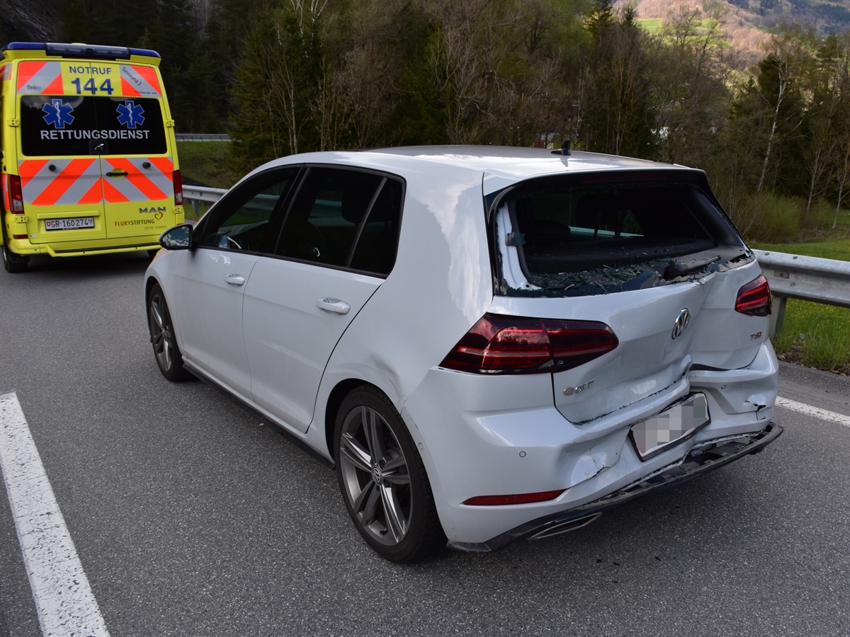 Das stark deformierte Heck und die linke hintere Seitenwand des Autos. Vor diesem steht der Rettungswagen. 