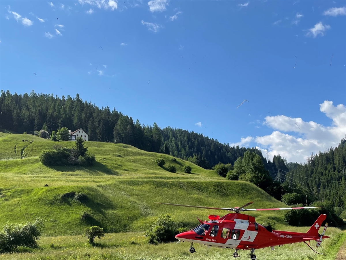 Unten rechts im Nahbereich der Rega-Helikopter. In der Ferne die ansteigende Wiese mit den Absturzspuren. Im Hintergrund blauer Himmel.