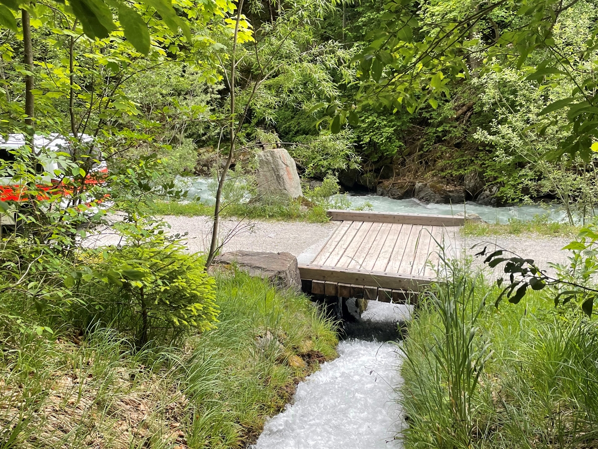 Der Trochabacha fliesst unter einer Holzbrücke in die Landquart. Links ein teilweise durch Gebüsch verdecktes Polizeiauto.