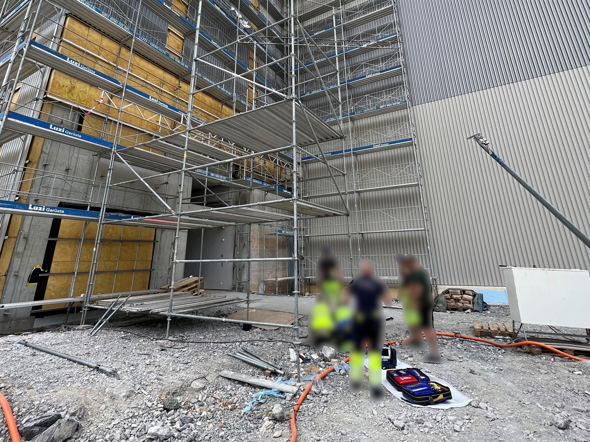 Baustellenbereich mit dem montierten Gerüst sowie der Plattform. Zusätzlich betreuen Arbeiter sowie das Ambulanzteam der Rettung Chur den auf dem Boden liegenden Verunfallten.