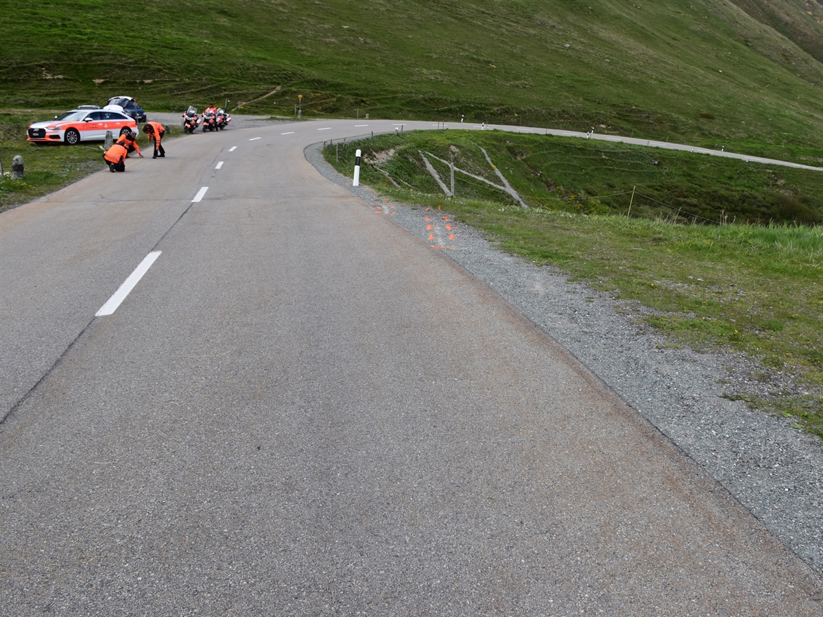 Verlauf der Strasse im Bereich der Unfallstelle. Links neben der Fahrbahn stehen ein Patrouillenfahrzeug sowie drei Polizeimotorräder. Einsatzkräfte der Kantonspolizei Graubünden sichern Spuren auf der Fahrbahn.