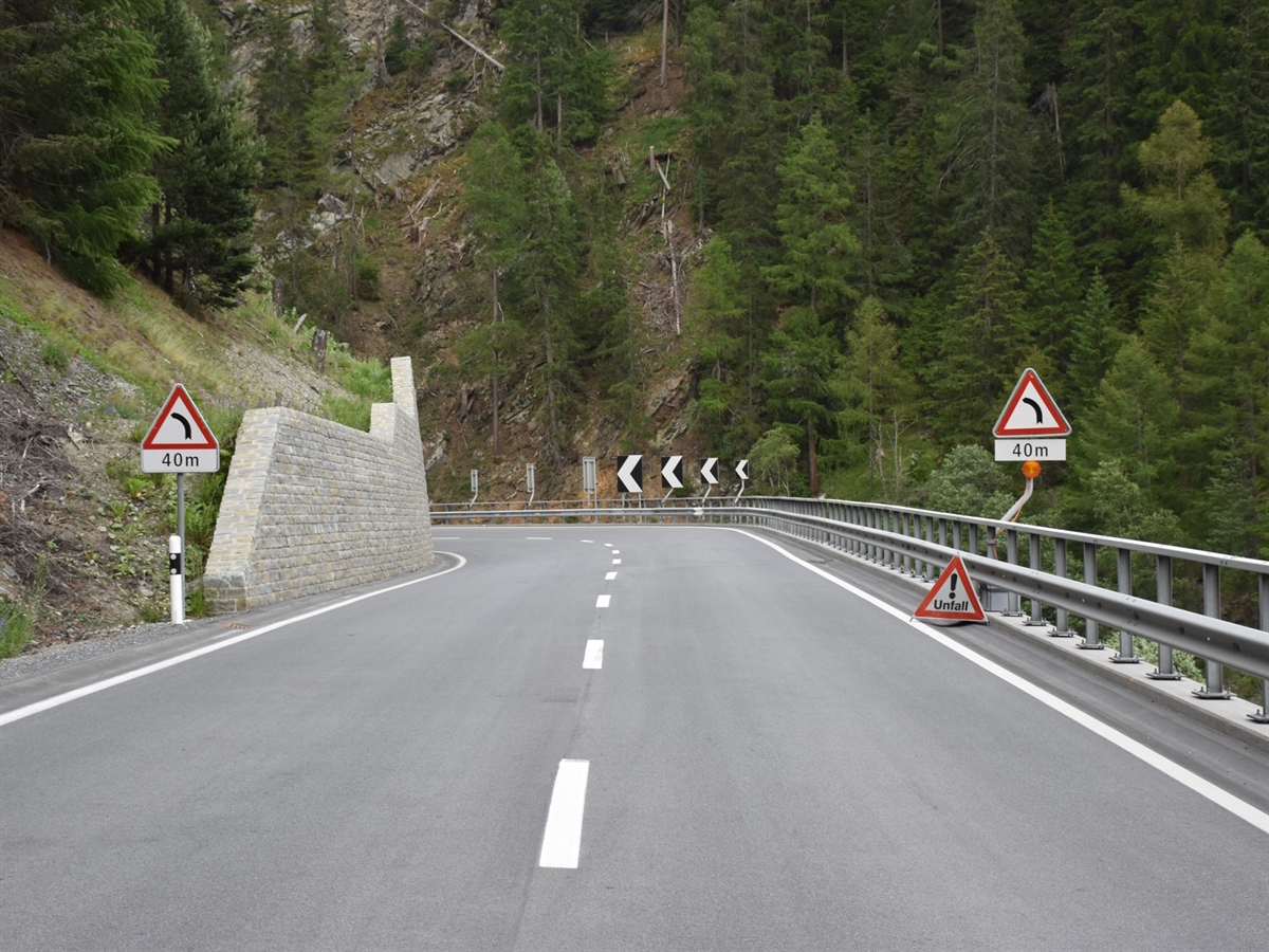 Eine Linkskurve, links und rechts der Strasse Gefahrensignale, in der Kurve selbst vier Leitpfeile nach links.