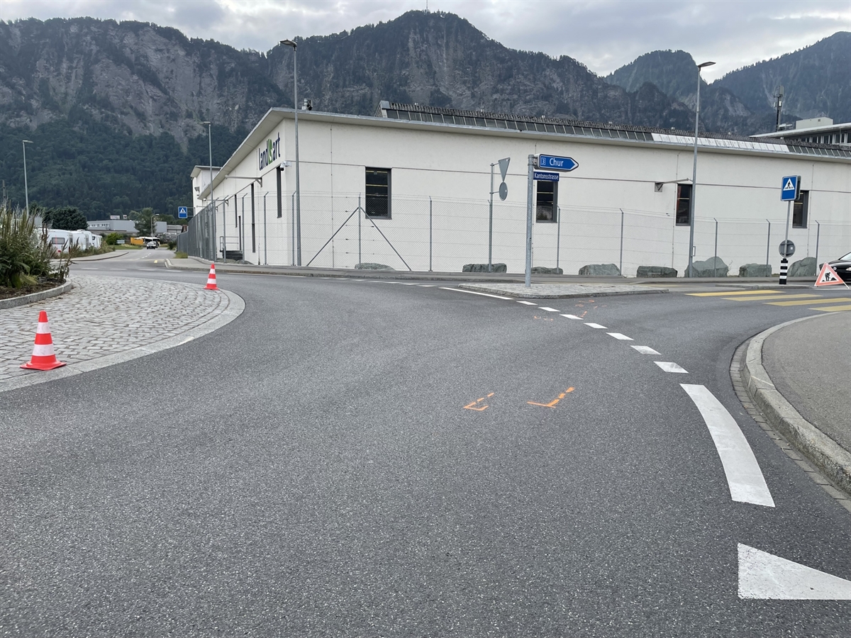 Der Kreisel mit Markierungen von Brems- und Kratzspuren auf der Fahrbahn. Im Hintergrund das Fabrikgebäude / Fabrikgelände.