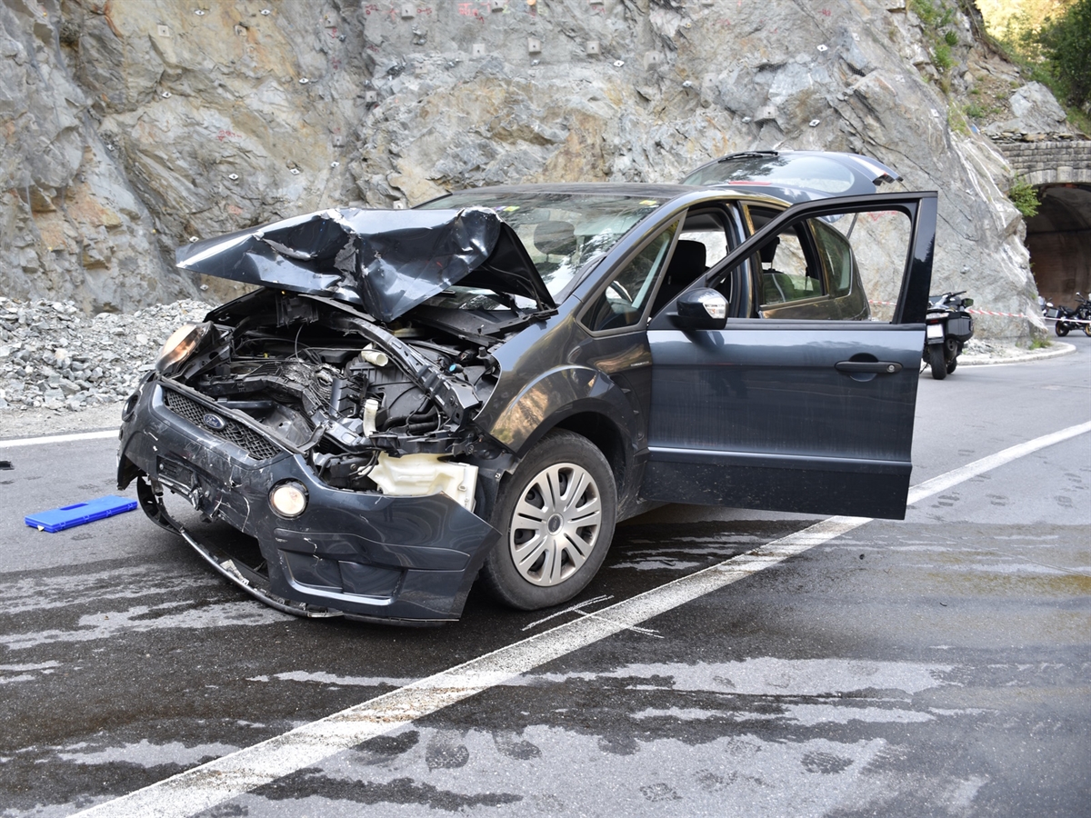 Von schräg vorne das an der Front stark beschädigte Auto. Im Hintergrund eine Felswand und ganz rechts ein Tunnelportal.