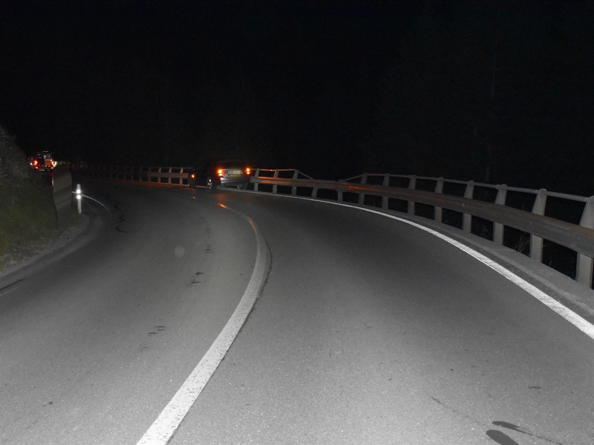 Die Linkskurve in der Nacht. Rechts die beschädigte Leitplanke und das daran stehende graue Unfallauto.