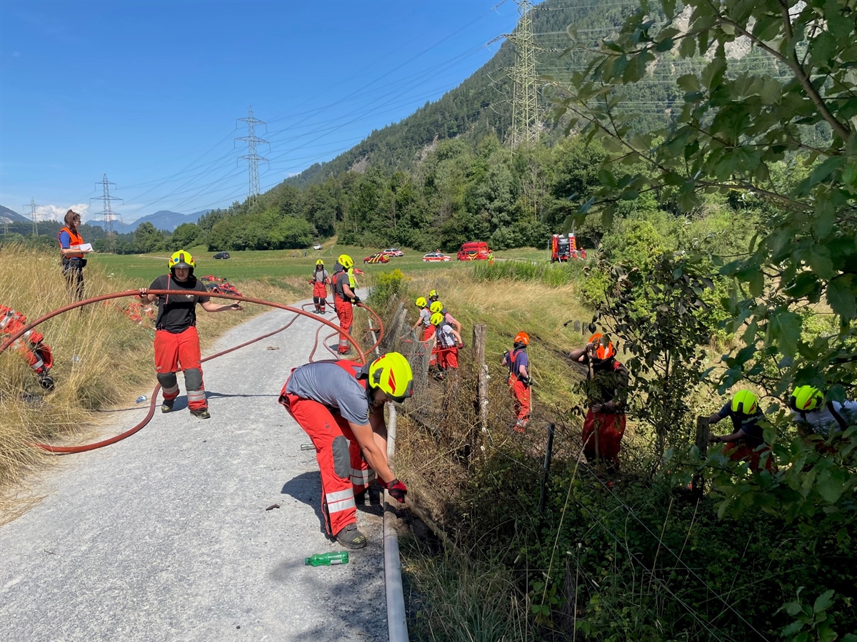 Feuerwehrleute mit Pickeln und Schläuchen am Wieshang
