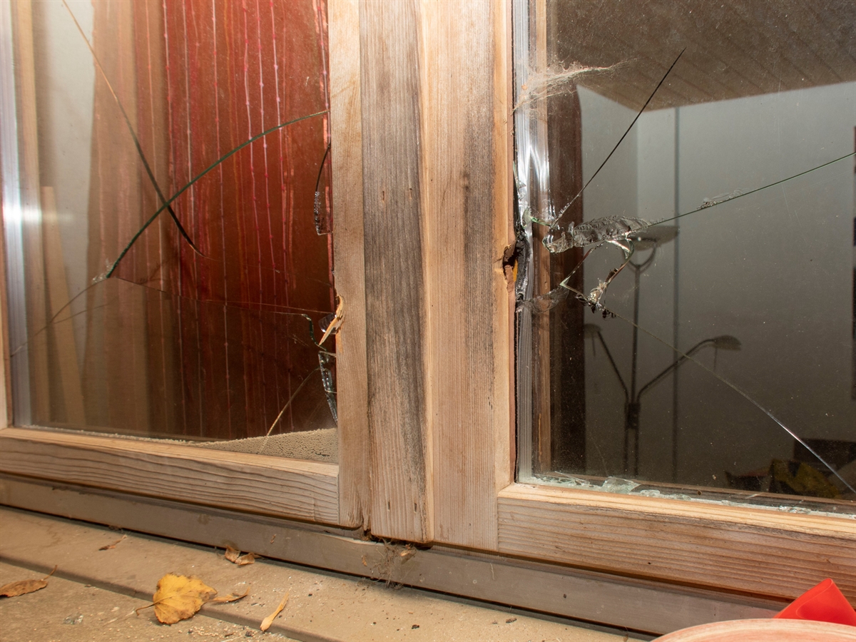Holzfenster mit eingeschlagenem Glas und sichtliche Einbruchspuren am Holzrahmen.