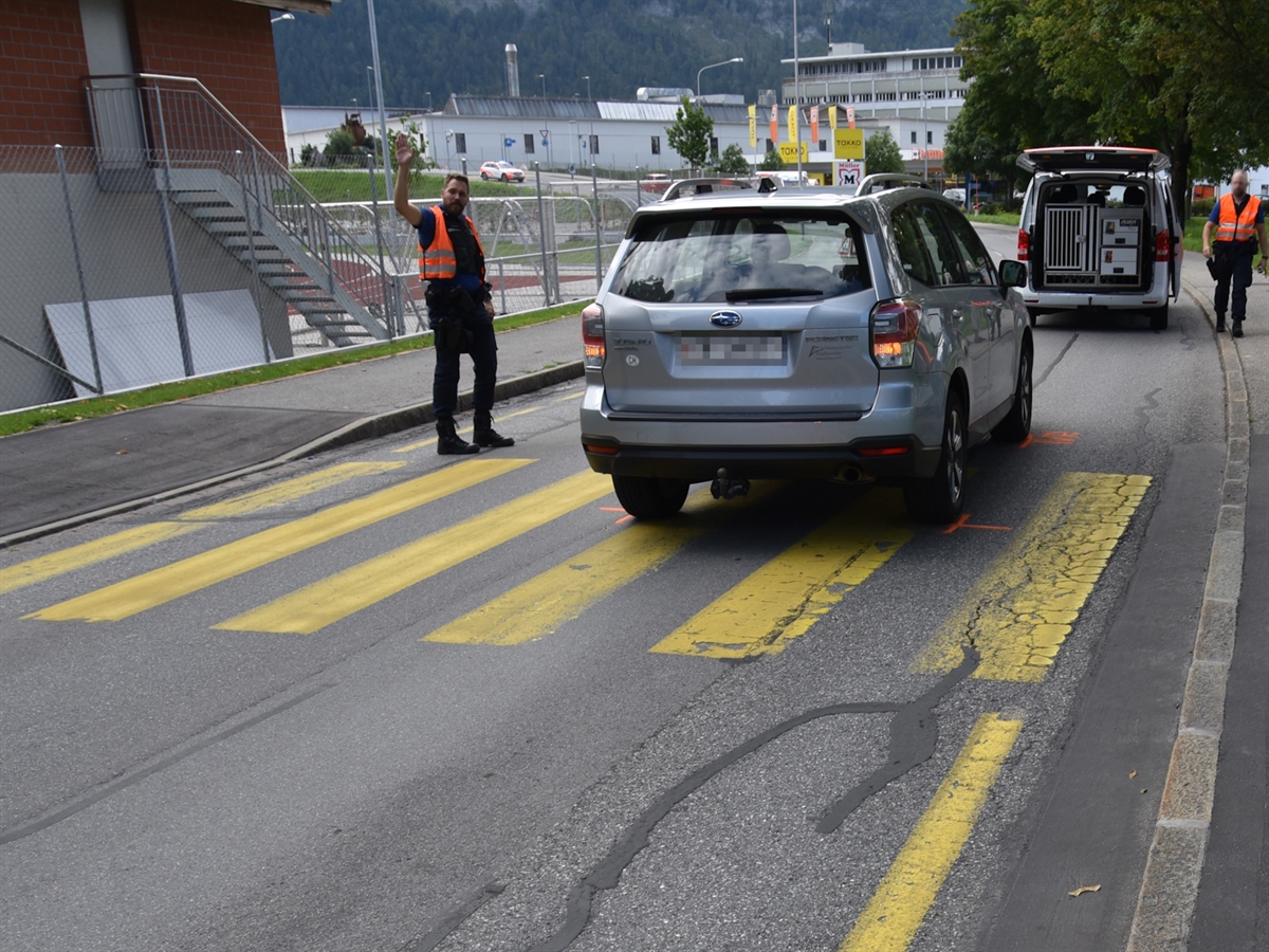 Das Auto steht mit dem Heck auf dem Fussgängerstreifen. Auf dem Trottoir steht ein Polizist neben einem Patrouillenfahrzeug. Ein weiterer Polizist regelt auf der Schulstrasse den Fahrzeugverkehr.