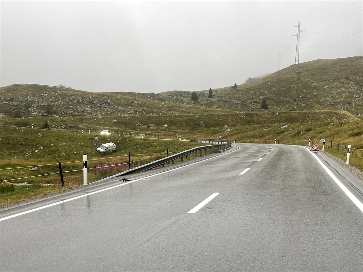 Die Gerade der Julierstrasse mit der anschliessenden Linkskurve, an welcher der Lieferwagen von der Strasse abkam. Dieser steht auf der grünen abfallenden Böschungswiese. Darüber auf der Fahrbahn ein Polizeifahrzeug.