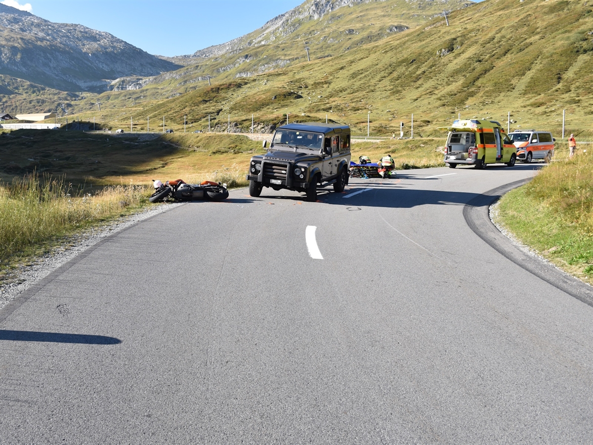 Eine Rechtskurve, auf der Strasse ein Polizeiauto, ein Rettungswagen sowie das am Unfall beteiligte Motorrad und das Auto. 