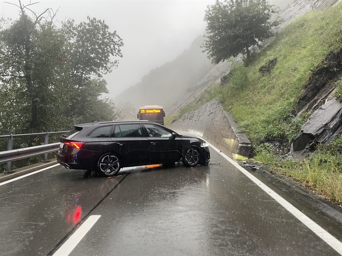 Das Auto mit stark beschädigter Front mitten auf der Strasse. Rechts eine Stützmauer, welche in eine steil ansteigende Böschung übergeht.