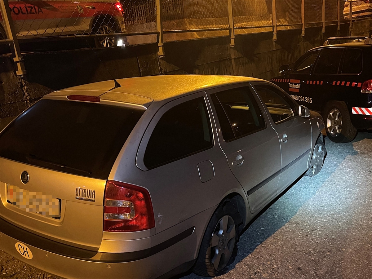Das Unfallauto von schräg rechts hinten. Die rechten Reifen sind platt. Im Hintergrund ein Ausschnitt eines Polizeiautos.