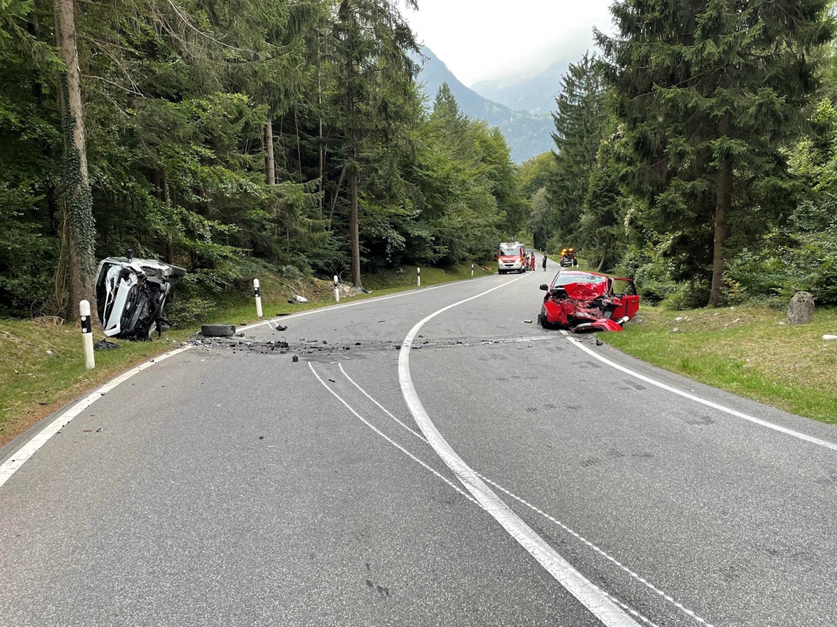 Unfallstelle: am rechten Strassenrand liegt das rote Auto komplett zerstört. Auf der linken Seite liegt auf der Seitenlage der weisse Lieferwagen. Weiter hinten im Bild stehen ein Einsatzfahrzeug und eine Ambulanz. Die Strasse weist eine leichte Rechtskurve auf und hat eine durchgezogene Mittellinie. Die Spuren sind mit weisser Kreide eingezeichnet.