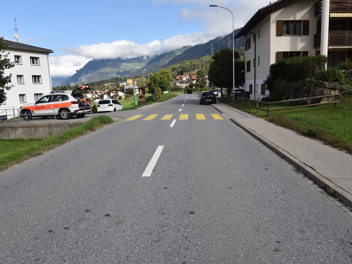 Links der Strasse ein Polizeiauto, mittig des Bildes ein Fussgängerstreifen. Die Strasse ist links und rechts durch Gebäude begrenzt.