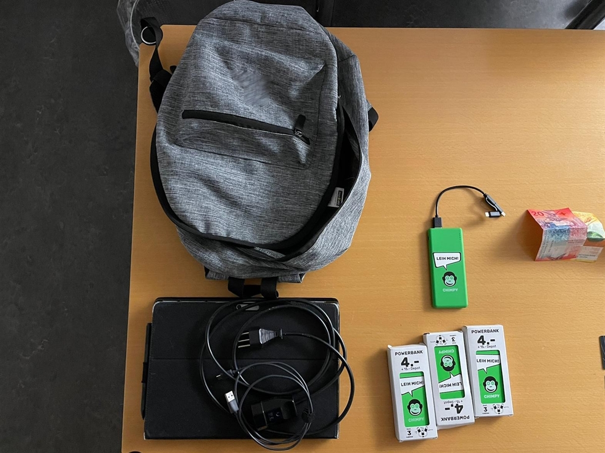 Aufnahme von oben: Auf einem Tisch sieht man einen Rucksack, Bargeld, ein Tablet und mobile Zusatzakkus.