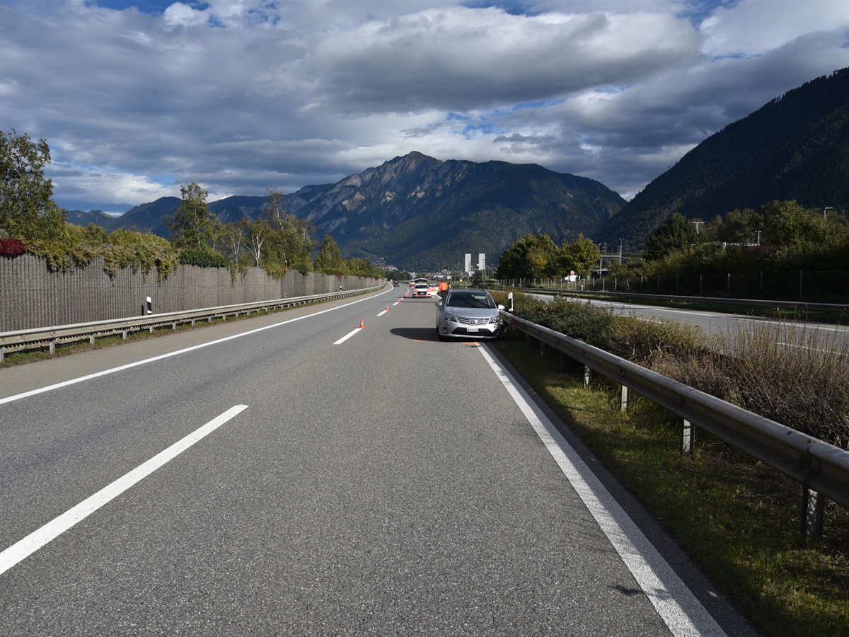 Das Unfallauto steht vorne links beschädigt auf der Überholspur an der Mittelleitplanke. Im Hintergrund steht ein Patrouillenfahrzeug auf der abgesperrten Überholspur. Das Herbstbild wird mit einem leicht bewölkten Himmel abgeschlossen.