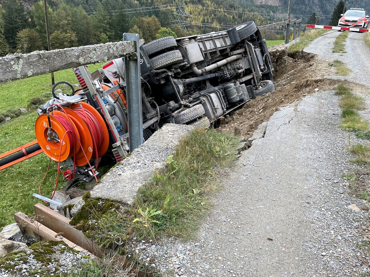 Die Naturstrasse mit der abgebrochenen Stützmauer, auf welcher der Lastwagen auf der Seite liegt. Im Hintergrund ein Patrouillenfahrzeug der Polizei.