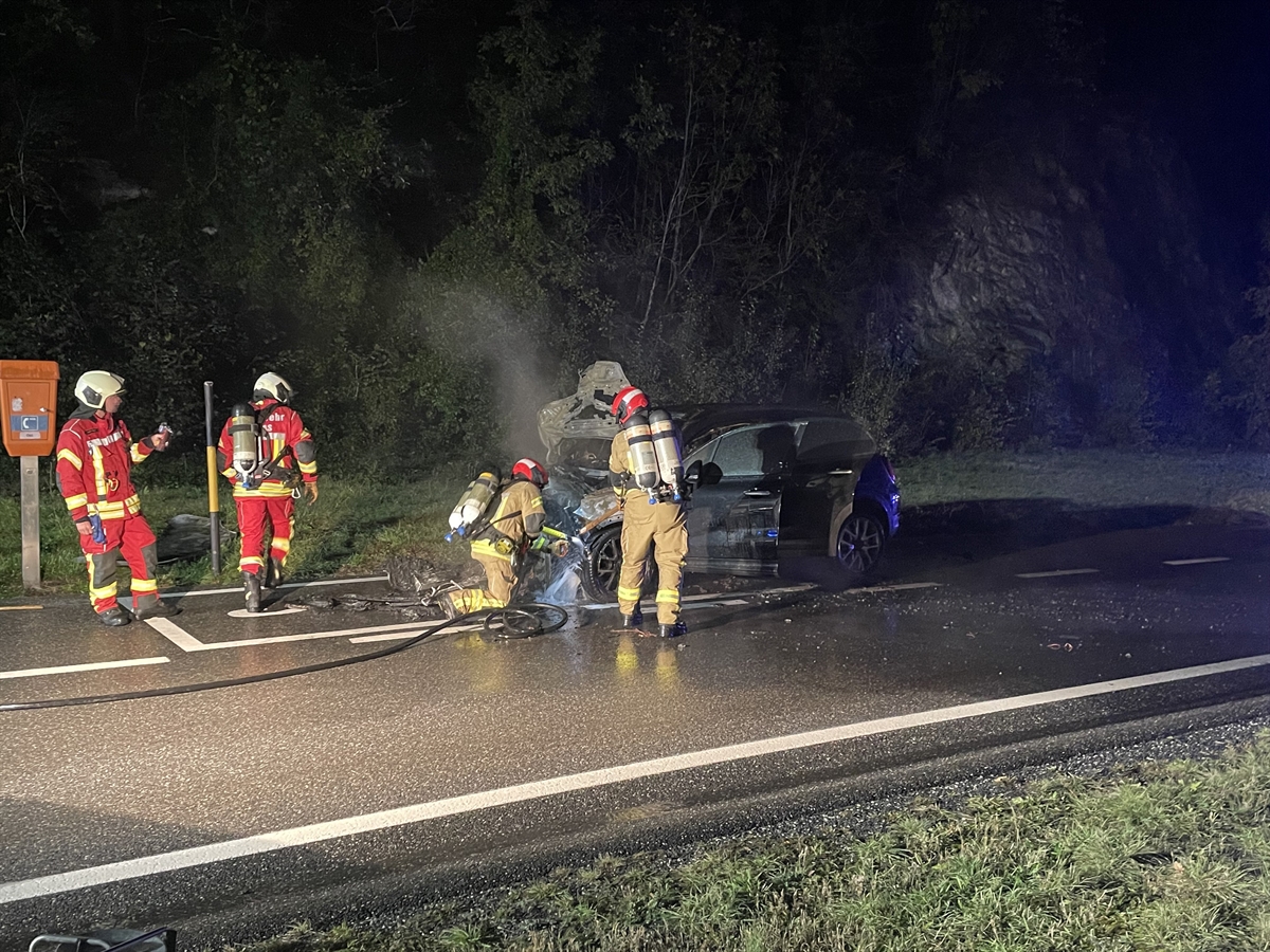 Feuerwehrleute in der Dunkelheit mit Löschgeräten beim ausgebrannten Auto
