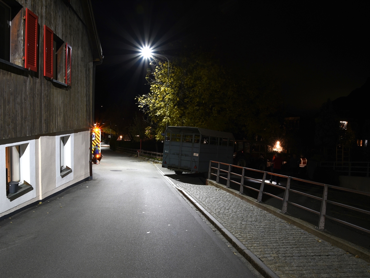 Aufnahme in der Dunkelheit. Eine Strassenlampe erhellt die Verzweigung. Ein Teil der Fahrzeugkombination steht noch knapp in der Verzweigung. Links ein Ambulanzfahrzeug.