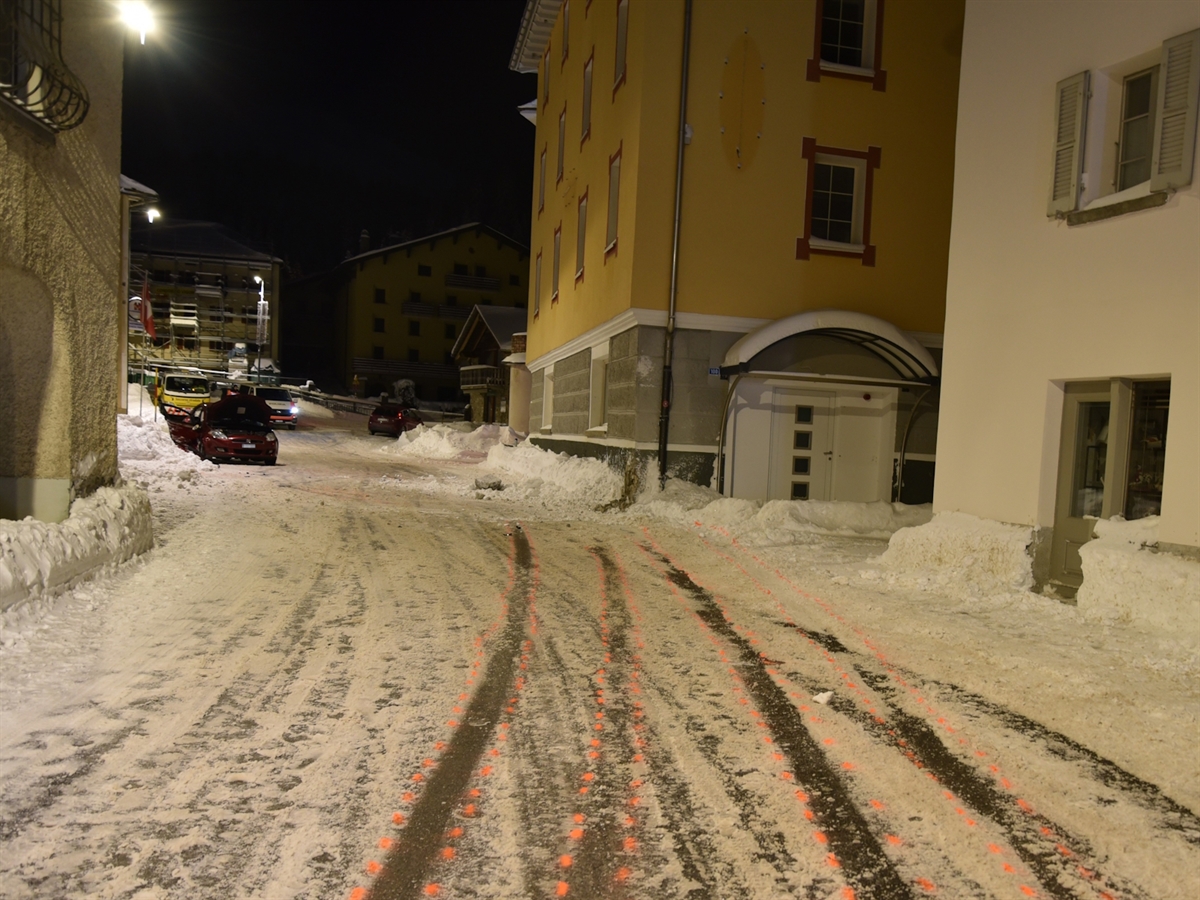 Nachtaufnahme. Schleuderspuren, die rechts an eine Hausecke und von dort zum links auf der Strasse stehenden total beschädigten Auto führen.