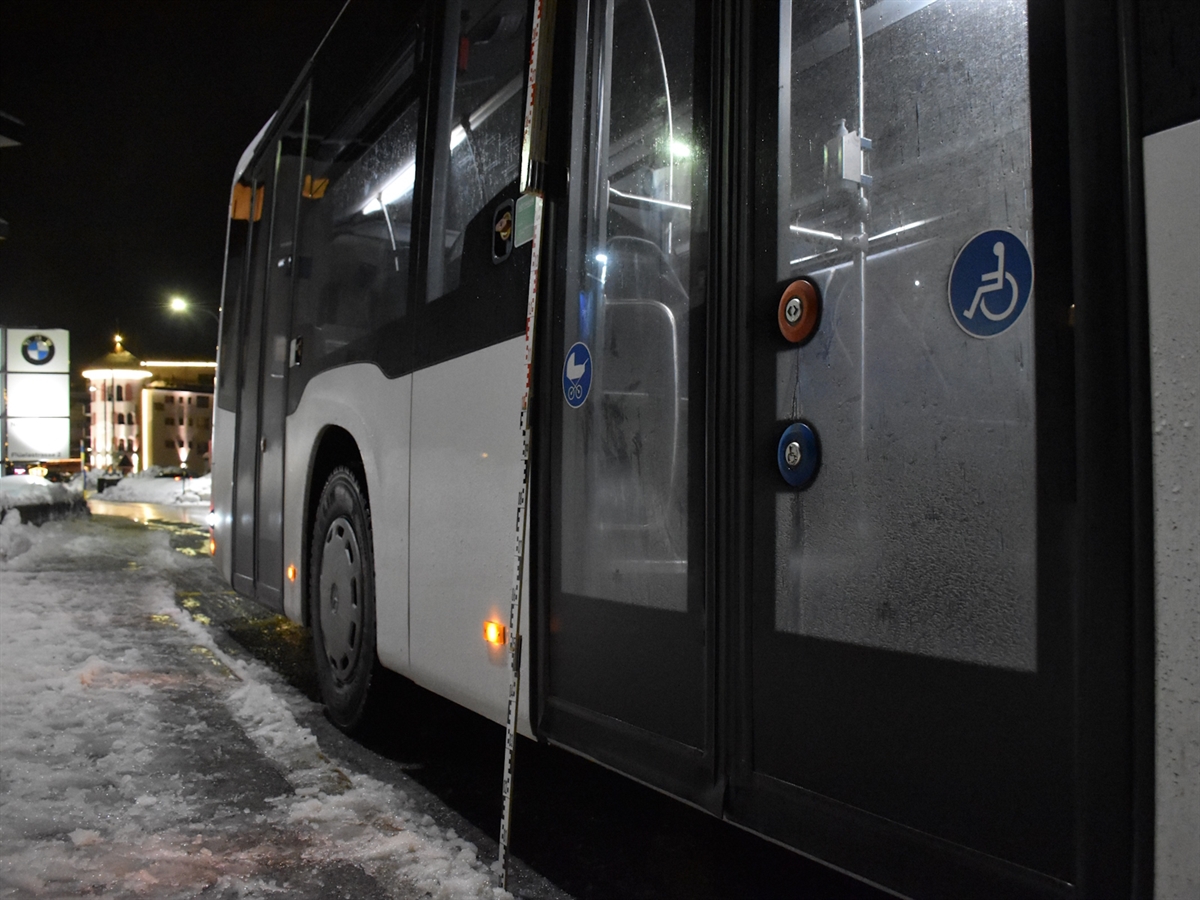 Die rechte Seite des Linienbusses, dieser steht in einer Bushaltebucht. Im Hintergrund Gebäude.