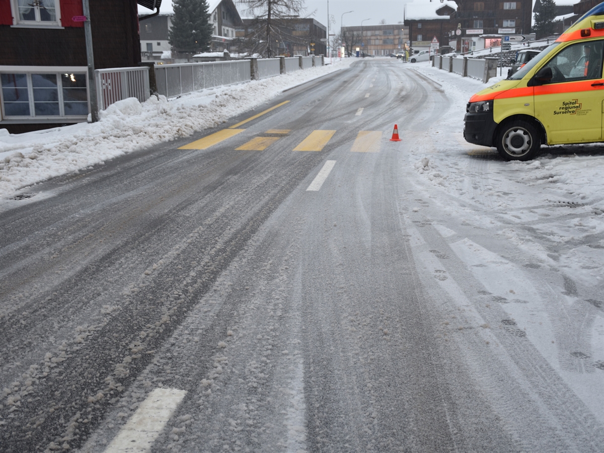 Die schneebedeckte Oberalpstrasse mit dem leicht erkenntlichen Fussgängerstreifen. Am rechten Bildrand ragt die Front des Rettungswagens in das Bild hinein.