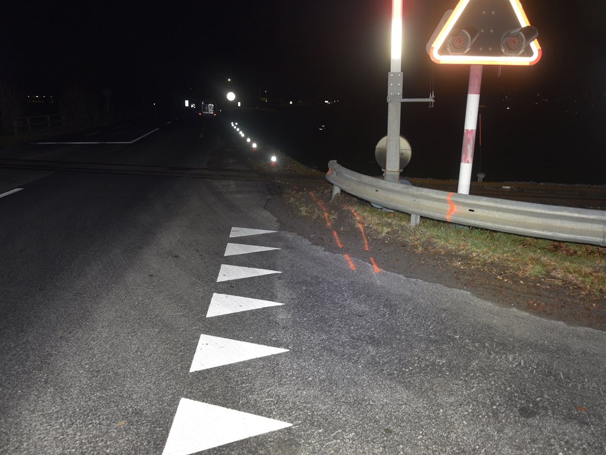 Leicht beschädigte Leitplanke beim Bahnübergang. Im Hintergrund ein Polizeifahrzeug sowie die reflektierenden Kontrollschilder des Autos im Wiesland