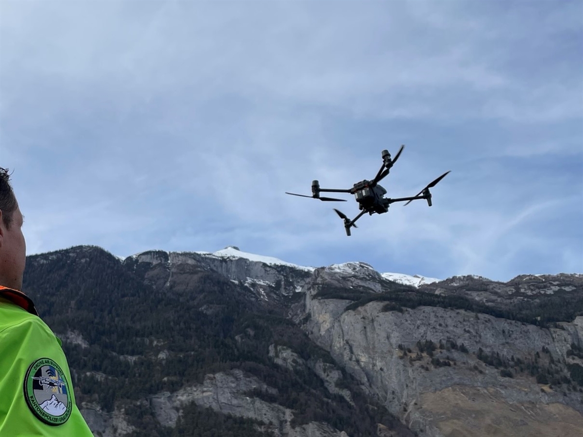 Himmel welcher sich von Gebirge abgrenzt. Eine fliegende Drohne im Blick eines sie steuernden Polizisten.